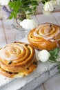 Freshly baked sweet bun with raisins on shabby white background with tender roses Royalty Free Stock Photo