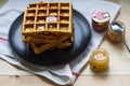 Freshly baked sweet delicious appetizing Belgian waffles with honey on a black plate on a wooden table. Royalty Free Stock Photo