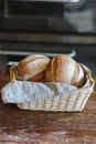 Freshly baked tasty rhye flour round loafs of rhye breads in wicker basket with grey linen kitchen towel at wooden table in bakery Royalty Free Stock Photo