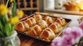 Freshly baked traditional cross buns for Happy Easter. Festive sweet pastries on rustic tray next to bright flowers Royalty Free Stock Photo