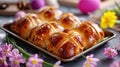 Freshly baked traditional cross buns for Happy Easter. Festive sweet pastries on rustic tray next to bright flowers Royalty Free Stock Photo