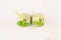 Freshly blended green kiwi fruit smoothie in glass jars with straw, mint leaf, top view.