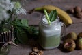 Freshly blended green and white smoothie in glass jar with stra