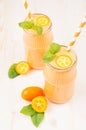Freshly blended orange citrus kumquat fruit smoothie in glass jars with straw, mint leaf, cute ripe berry, close up.
