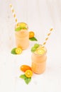 Freshly blended orange citrus kumquat fruit smoothie in glass jars with straw, mint leaf, cute ripe berry, copy space.