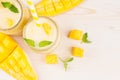 Freshly blended yellow mango fruit smoothie in glass jars with straw, mint leaves, mango slices, close up, top view.