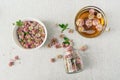 Freshly brewed herbal clover tea in glass mug, heap of flowerheads on light gray background, top view