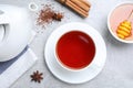 Freshly brewed rooibos tea, scattered dry leaves, honey and spices on grey table, flat lay