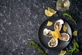 Freshly caught, opened oysters on a black plate with lemon slices, herbs and a glass of champagne on a dark stone background.