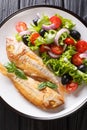 Freshly cooked pink dorado fish with lemon and vegetable salad close-up on a plate. Vertical top view