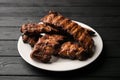 Freshly cooked pork ribs on a white round plate on a black wooden table in the background. Close-up, 45 degree angle Royalty Free Stock Photo