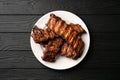 Freshly cooked pork ribs on a white round plate on a black wooden table in the background. Close up, top view. Royalty Free Stock Photo