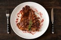 Freshly cooked t-bone steak sprinkled with spices and garnished with a sprig of rosemary on a round white plate with a fork knife Royalty Free Stock Photo