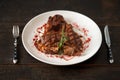 Freshly cooked t-bone steak sprinkled with spices and garnished with a sprig of rosemary on a round white plate with a fork knife Royalty Free Stock Photo