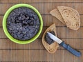 Freshly cooked tapenade in a green bowl, several slices of bread and a knife