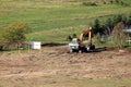 Freshly flattened and cleaned local construction site with single excavator parked after work surrounded with partially dry grass