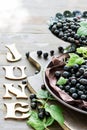 Freshly gathered big juicy black currants on brown plate closeup, word June of wooden letters on a table, berries outdoors, in gar