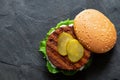 Freshly grilled plant based burger patty in bun with lettuce, slices of gherkin  and sauce isolated on black slate. Top view. Copy Royalty Free Stock Photo