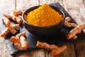 Freshly ground turmeric in a black bowl and fresh root close-up. horizontal