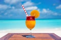 Freshly made colorful tropical fruity cocktail with straw and slice of orange on wooden table ocean background at the beach Royalty Free Stock Photo