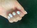 Freshly manicured nails in a white colour on a dark green velvet cushion