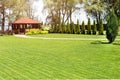 Freshly mowed rows of green lawn at country residence with summerhouse. Hedge of fresh cedars. Landscape design and