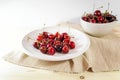 Freshly picked cherries in a ceramic plate and bowl with a napkin on a light wooden table, tasty summer snack, copy space Royalty Free Stock Photo