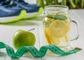 Freshly prepared drink of lemon, measuring tape and mint on the background of sports shoes.