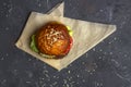 Freshly prepared grilled beef burger with lettuce and tomato served on pieces of parchment paper on a dark background. Copy space Royalty Free Stock Photo