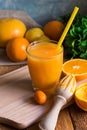 Freshly pressed citrus fruit juice from oranges lemons limes cumquat, glass with straw, reamer, mint on table by window, rustic Royalty Free Stock Photo