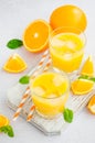 Freshly squeezed orange juice with ice in a glass with a straw on a wooden board on a light background with fresh oranges. Royalty Free Stock Photo