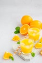 Freshly squeezed orange juice with ice in a glass with a straw on a wooden board on a light background with fresh oranges. Royalty Free Stock Photo