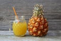 Freshly squeezed pineapple juice in a glass cup with drinking straw and ripe ananas fruit on old wooden table. Royalty Free Stock Photo