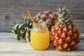 Freshly squeezed pineapple juice in a glass cup with drinking straw and ripe ananas fruits on old wooden table. Royalty Free Stock Photo