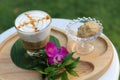 Glass of hot caramel macchiato coffee with cookie and orchid flower on wooden plate in coffee shop of Thailand.