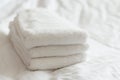Freshly washed white hand towels stacked on a white bed.
