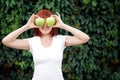 Freshness, healthy lifestyle, vitamines and nutrition concept: smiling woman with red hair hiding her eyes behind two green apples