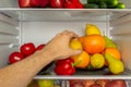 Fridge is filled with vegetables, fruits. Hand takes food from the refrigerator Royalty Free Stock Photo