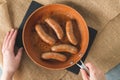 Fried bratwurst pork sausages on a frying pan close-up on the kitchen table, view from above, copy space, woman hands Royalty Free Stock Photo