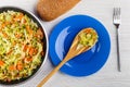 Fried cabbage with carrot, green peas in frying pan, bread, spoon with cabbage in plate, fork on table. Top view Royalty Free Stock Photo