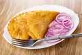Fried cheburek, rings of red onion, fork in dish on wooden table