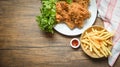 Fried chicken crispy and salad lettuce on white plate with french fries basket ketchup on wooden dining table