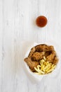 Fried chicken drumsticks, spicy wings, French fries and tender strips in paper box and sauce over white wooden background, overhea