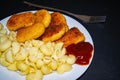 Fried chicken nuggets and boiled pasta with ketchup on a white plate on a dark background. Close up