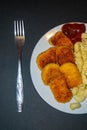 Fried chicken nuggets and boiled pasta with ketchup on a white plate on a dark background. Close up Royalty Free Stock Photo
