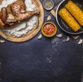 Fried chicken with rice on a cutting board, hot sauce, spices, garlic and corn in the pan on dark blue wooden rustic background to
