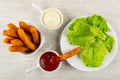 Fried chicken sticks in bowl, sauce boats with mayonnaise, ketchup, chicken stick in sauce, plate with lettuce on wooden table. Royalty Free Stock Photo