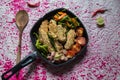 Fried chicken and stir fried vegetables in a black frying pan.