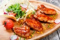 Fried chicken wings with fresh salad, grilled vegetables and bbq sauce on cutting board on wooden background close up Royalty Free Stock Photo