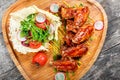 Fried chicken wings with fresh salad, grilled vegetables and bbq sauce on cutting board on wooden background